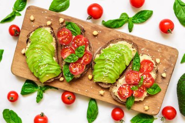 Avokado tost. Avokado, kiraz domates, fesleğen ve susam tohumu ahşap kesme tahtası üzerinde sağlıklı tost. üstten görünüm