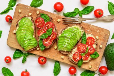 avokado, domates, fesleğen, humus ve susam tohumu rustik kesim üzerinde sandviçle beyaz mermer masa üzerinde kurulu. Sağlıklı kahvaltı. üstten görünüm