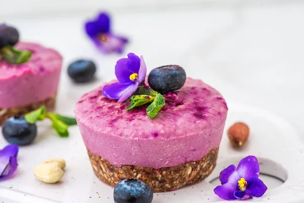 blueberry and acai vegan cashew cakes with fresh berries, edible flowers, mint, nuts. healthy vegan food concept. close up