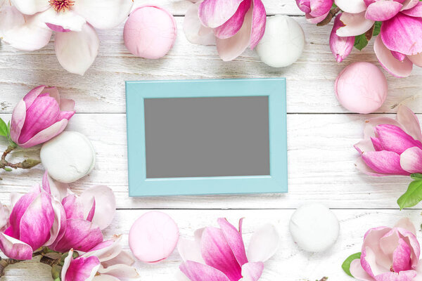blank photo card in frame made of pink magnolia flowers and marshmallows on white wooden background. flat lay. top view. mock up. wedding or womens day composition