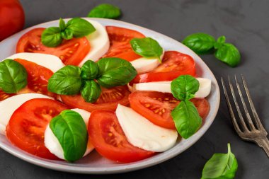 olgun domates ve mozzarella peyniri ile caprese salatası, koyu beton arka plan üzerinde taze fesleğen yaprakları. İtalyan yemekleri