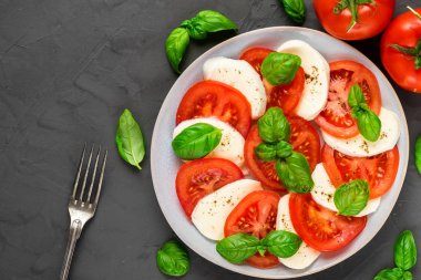 dilimlenmiş domates, mozzarella peyniri, fesleğen, biber ve çatal ile taze İtalyan caprese salatası bir tabakta