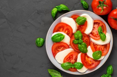 olgun domates ve mozzarella peyniri ile caprese salatası, koyu beton arka plan üzerinde taze fesleğen yaprakları. İtalyan yemekleri