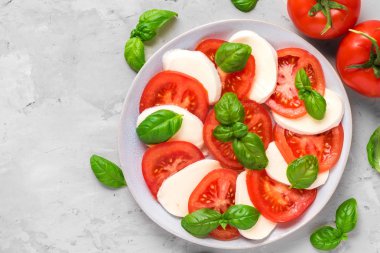 olgun domates ve mozzarella peyniri ile caprese salatası, beton arka plan üzerinde taze fesleğen yaprakları. İtalyan yemekleri