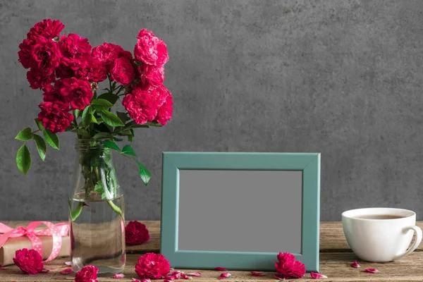 Leerer Fotorahmen und Rosenblüten mit Tasse Tee und Geschenkbox auf rustikalem Holztisch. Attrappe. Stillleben — Stockfoto