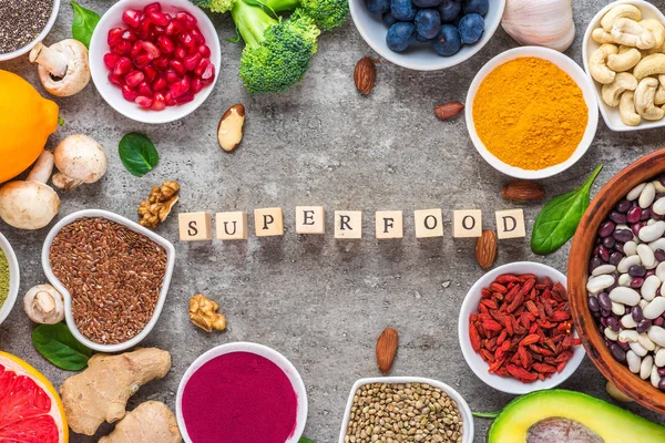 frame of superfood clean eating selection: fruit, vegetable, seeds, superfood, nuts, berries on concrete background