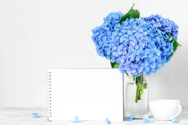 Κενή ευχετήρια κάρτα και μπλε ορτανσίες λουλούδια με φλιτζάνι καφέ σε λευκό ξύλινο τραπέζι. μακέτα — Φωτογραφία Αρχείου