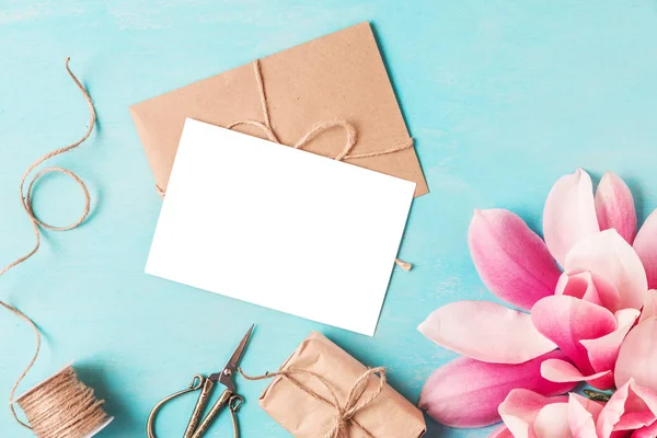 Tarjeta de felicitación en blanco, flores de magnolia rosa en cono de gofre y caja de regalo sobre fondo azul pastel. plano laico . — Foto de Stock