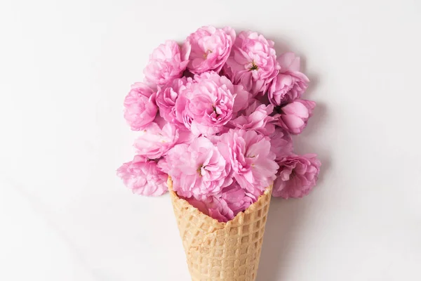 Bunga ceri merah muda mekar di es krim kerucut pada latar belakang putih. latar belakang pernikahan atau liburan — Stok Foto