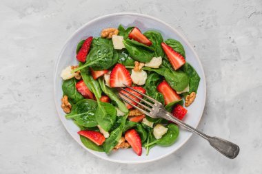 çilek, parmesan peyniri ve beton arka plan üzerinde bir çatal ile ceviz ile yaz ıspanak salatası kase