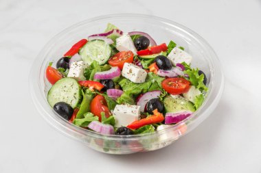Beyaz mermer arka plan üzerinde götürmek veya gıda teslimat ı için plastik paket sağlıklı yunan salatası