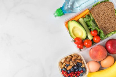 sandviç, sebze, fındık, çilek, muz, yumurta, avokado, şeftali ve su ile sağlıklı öğle yemeği kutuları