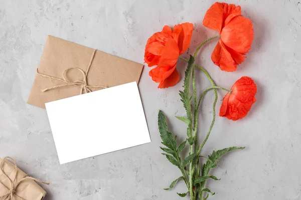 Blank gratulationskort, presentförpackning och kuvert med röd vallmo blommor bukett på betong bakgrund. Flat Lay — Stockfoto