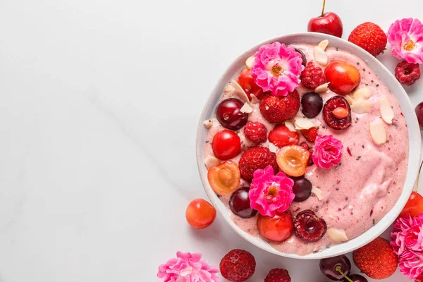 smoothie bowl or nice cream made of frozen bananas and berries with fresh berries, rose flowers, nuts and