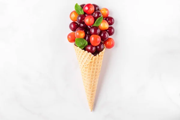 Buah ceri dengan mint dalam wafel es krim kerucut pada latar belakang marmer putih. Konsep makanan musim panas. tampilan atas — Stok Foto