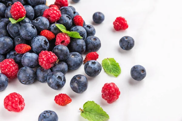 wild berries blueberry, strawberry and raspberry with mint on white marble background. summer food concept