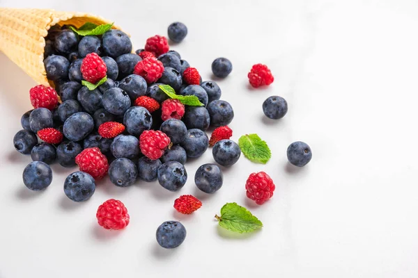 wild berries blueberry, strawberry and raspberry with mint in waffle ice cream cone on white marble background.