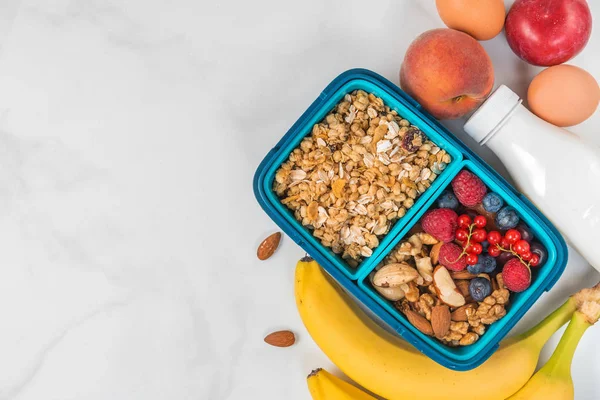 Healthy lunch box with granola, nuts, berries, banana, eggs, peaches and yogurt to make breakfast on white background