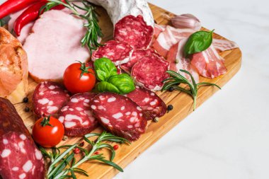 Salam, dilimlenmiş jambon, sosis, pastırma. Beyaz mermer masada sebzeli ve otlu et antipasto tabağı