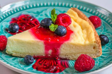 Taze ahududu, yaban mersini, reçel ve naneli bir dilim peynirli kek mermer arka planda mavi bir tabakta. Kapat.