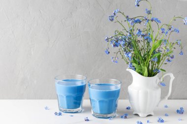 Mavi bezelyeli latte ve bir buket mavi çiçekli iki bardak beton kaplama vazoda beni unutma. Durgun hayat. Tatil arkaplanı