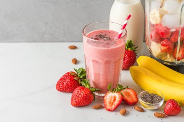 Bir bardak çilekli ve muzlu vejetaryen smoothie ya da badem sütünden yapılmış sağlıklı bir içecek yapmak için taze sulu malzemelerle karıştırılmış milkshake. Yemek pişirme konsepti