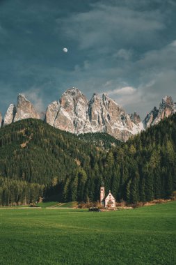Beautiful view of church Saint John in Ranui in Italian village Santa Maddalena in Dolomites Alps at sunset. Val di Funes, South Tyrol, Italy, Europe. Vertical orientation clipart