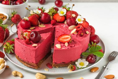 Çiğ vejetaryen dilimlenmiş çilekli cheesecake, kaju, kiraz, çilek, hindistan cevizi, badem ve taze böğürtlen ve çiçeklerle dolu hurma. Lezzetli tatlı. Kapat.