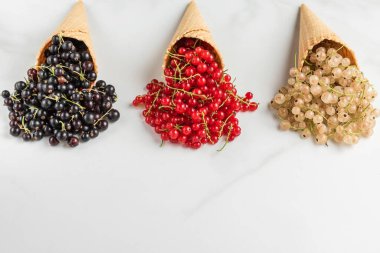 Beyaz mermer arka planda kremalı dondurma külahında üzümlü üzümler. Kırmızı, siyah ve beyaz frenk üzümü. Taze yaz meyveleri. Kapat.