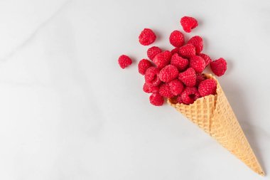 Beyaz mermer arka planda waffle dondurma külahında taze yaz ahududu. Yaz yemeği konsepti. Düz yat. Kopyalama alanı olan üst görünüm