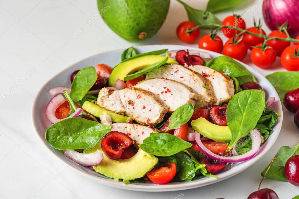 Healthy summer salad with grilled chicken breast, avocado, spinach, cherry berries and tomato on white background. healthy diet food. close up