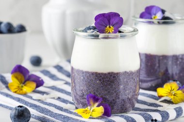 Taze böğürtlenli, hindistancevizli yoğurtlu, chia pudingli ve yenilebilir çiçekli sağlıklı vejetaryen kahvaltısı.