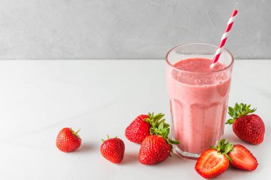 Çilekli milkshake ya da beyaz arka planda pipetli ve taze meyveli bir bardakta smoothie. Yaz içeceği. Sağlıklı diyet yemekleri