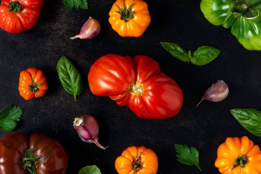 Renkli organik domateslerden yapılmış domatesler fesleğen, siyah arka planda sarımsak. Üst Manzara. Düz yat. Vegan diyet yemek pişirme konsepti