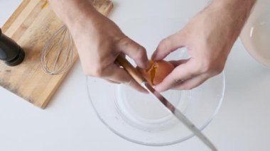 Çiğ yumurtayı beyaz masada süt ve biber öğütücüyle cam kaseye kıran bir adam kahvaltı hazırlıkları sırasında. Omlet ya da çırpılmış yumurta. Sağlıklı yiyecekler. Üst görünüm.