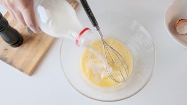Kahvaltı hazırlıkları sırasında cam kaseye süt döken ve çırpılmış yumurta çırpan bir adam. Omlet ya da çırpılmış yumurta. Sağlıklı yiyecekler. Üst görünüm.