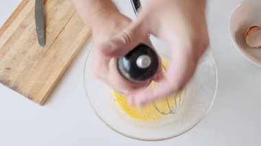 Kahvaltı hazırlıkları sırasında baharat ve çırpılmış yumurtaları cam kasede biber öğütücüyle mutfakta süt ile çırpan bir adam. Omlet ya da çırpılmış yumurta. Sağlıklı yiyecekler. Üst görünüm.