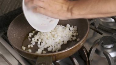 Chopped white onions being added to hot oil in frying pan on stovetop during meal preparation. Cooking food process on gas stove at home. Everyday culinary preparation.