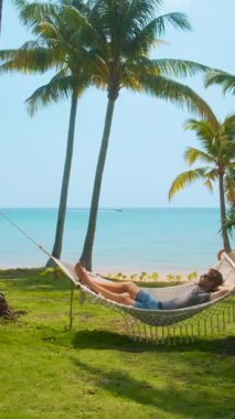 Turkuvaz deniz ve yeşil çimen ile tropik sahildeki palmiye ağaçlarının arasında dinlenen bir adam, rahatlama, yaz tatili ve huzurlu bir kaçış için cennet, Phu Quoc Adası, Vietnam