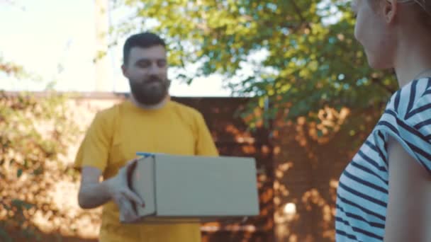 Brevbäraren levererar ett paket för en ung kvinna — Stockvideo