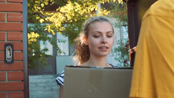 Der Postbote liefert ein Paket für eine junge Frau aus — Stockvideo