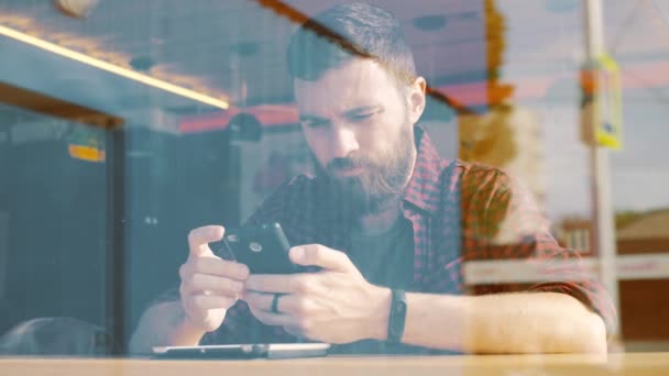 Ο άνθρωπος χρησιμοποιώντας app στο smartphone στο café. Πυροβόλησε μέσα από το παράθυρο — Αρχείο Βίντεο