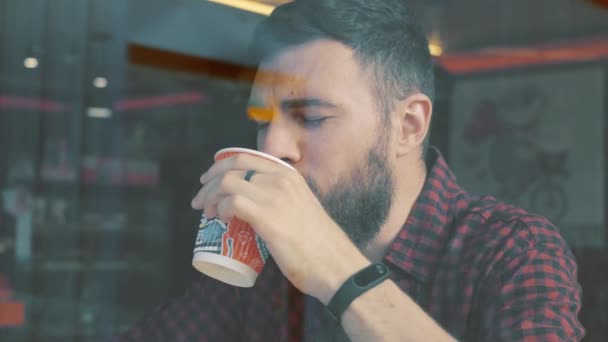 Bir kadeh bir akıllı telefon ile kafede oturan bir adam. Shot Cafe aracılığıyla penceresini göster. — Stok video