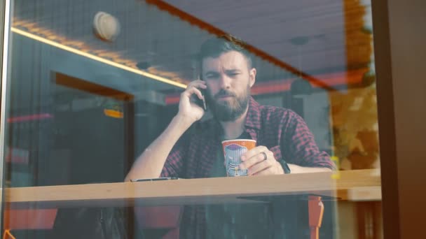 Junge Brünette ruft im Café am Fenster an und trinkt Kaffee — Stockvideo