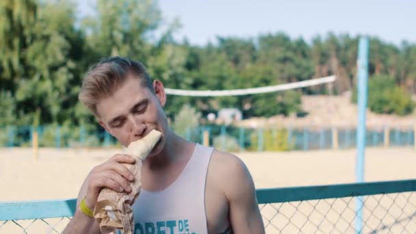 Primer plano del hombre guapo comiendo shaurma en una cancha de voleibol — Vídeos de Stock