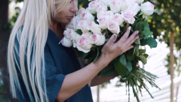 Ein schönes Mädchen schnuppert Rosen in einem Strauß — Stockvideo