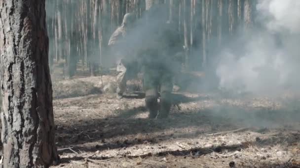 Повністю обладнані солдати під ворожого нападу, стрибають через курган у димчастому лісі — стокове відео