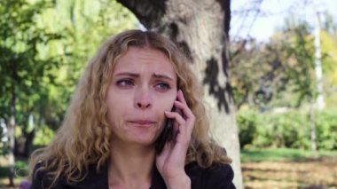 parkta bir bankta oturmuş telefonda konuşan ağlayan kız