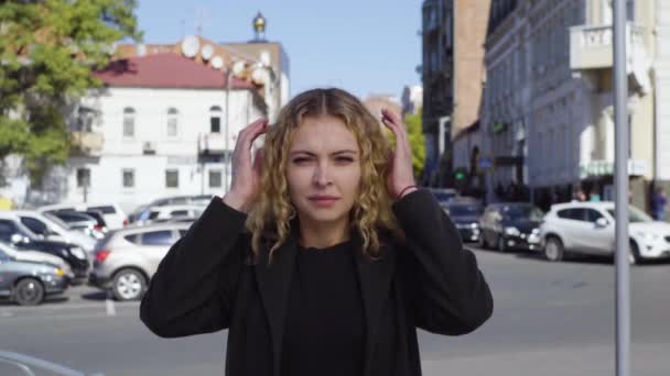 Mujer rubia gritando cubriéndose los oídos con los ojos cerrados en la calle de la ciudad — Vídeos de Stock