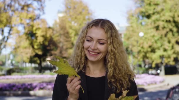 Jovem com folhas de bordo em pé em um parque de outono — Vídeo de Stock